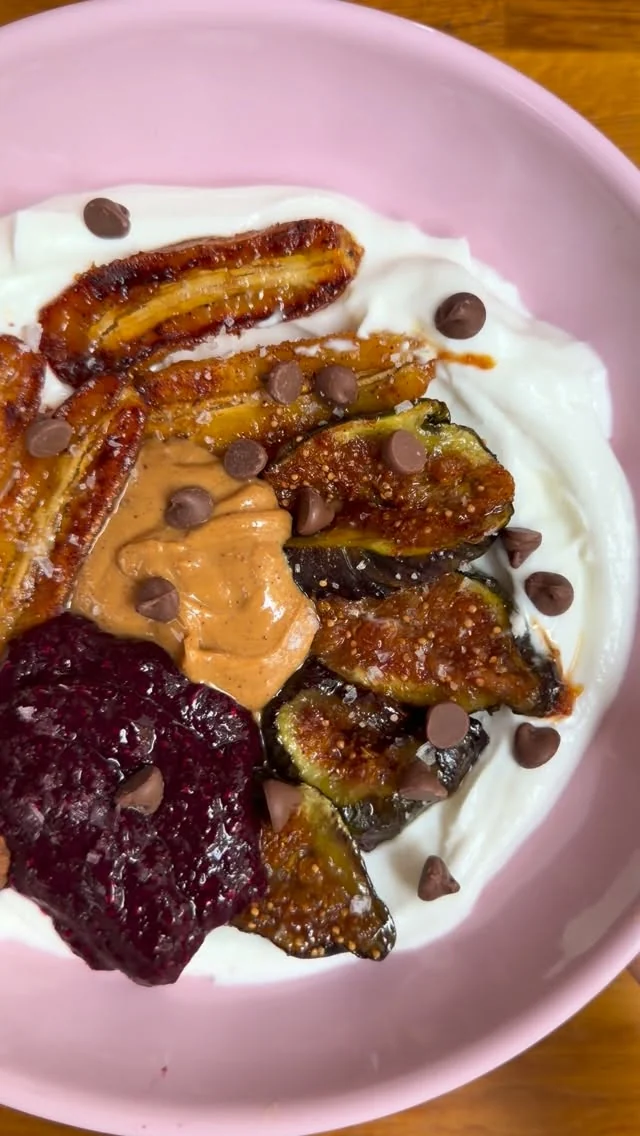 Yogurt bowl with caramelised bananas, fresh figs, blueberry jam and peanut butter on a pink plate