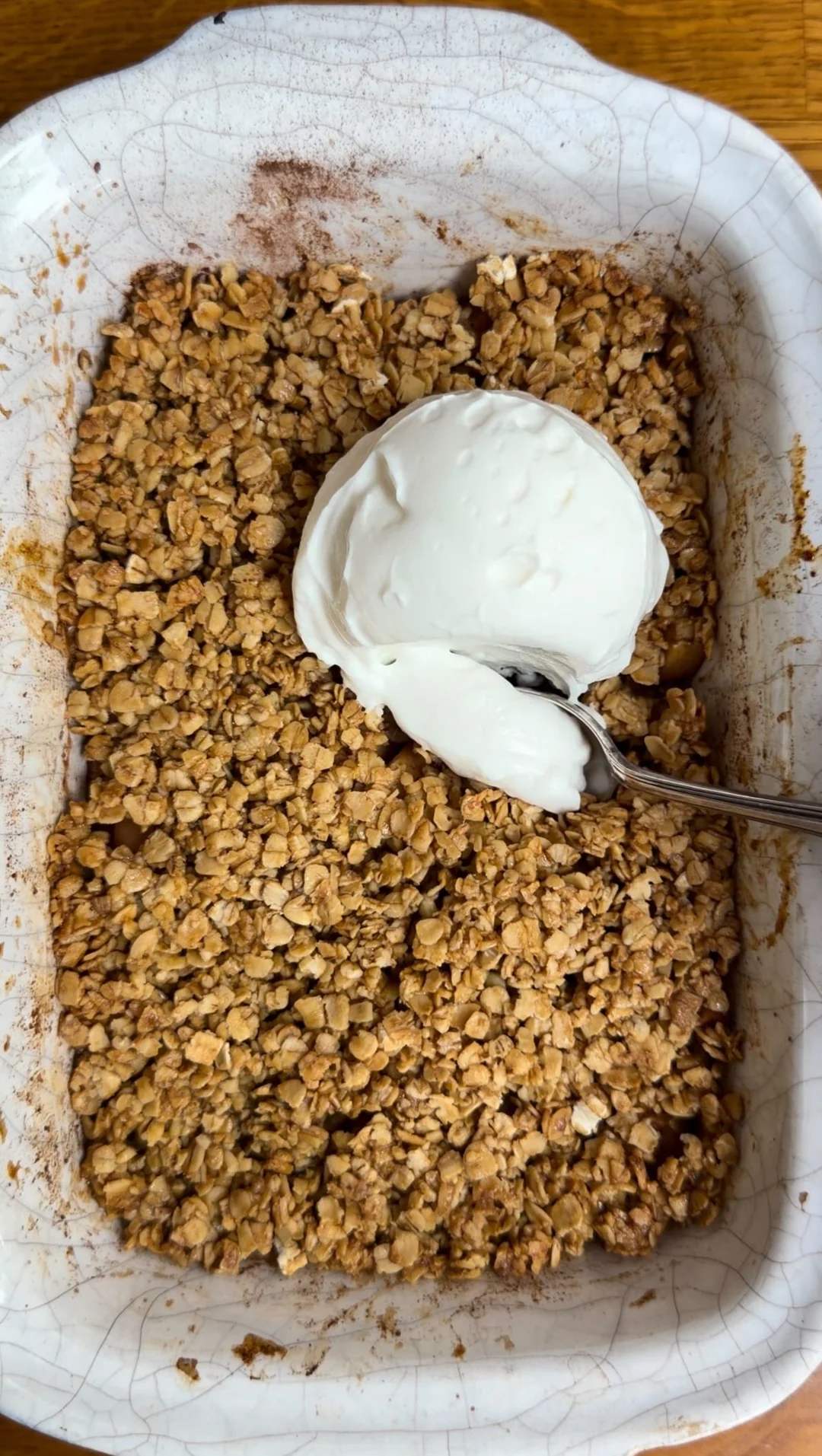 Apple crumble in a white baking dish with a spoonful of yogurt