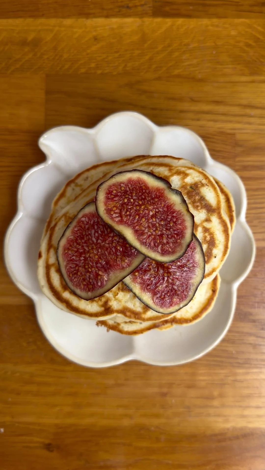 Golden pancakes topped with sliced figs on a scalloped plate