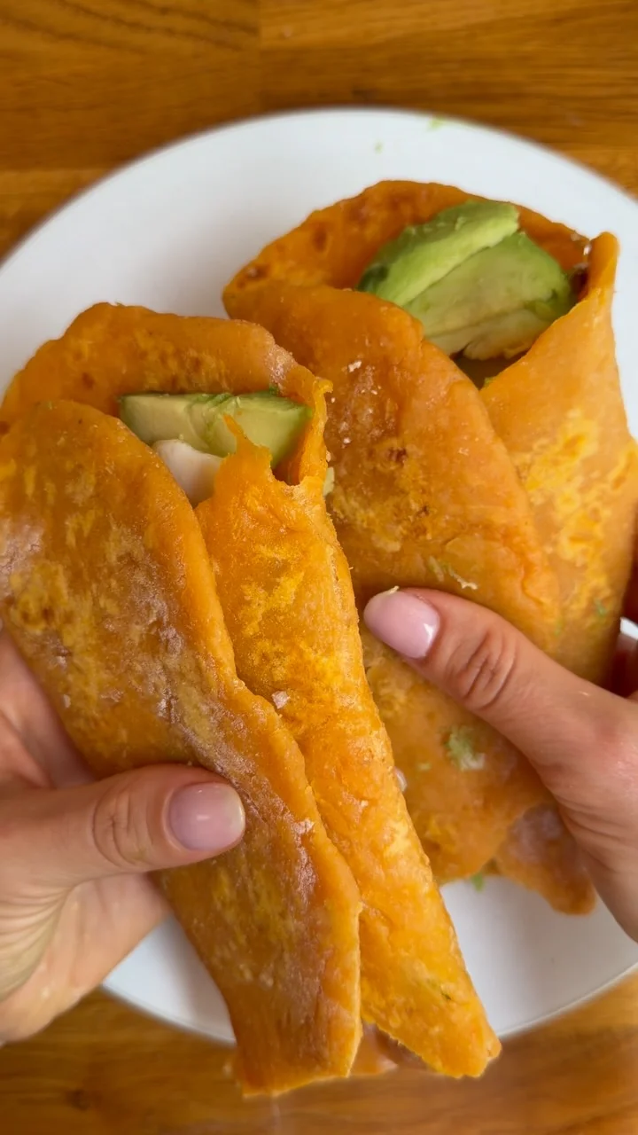 Hands holding sweet potato wraps filled with avocado and egg